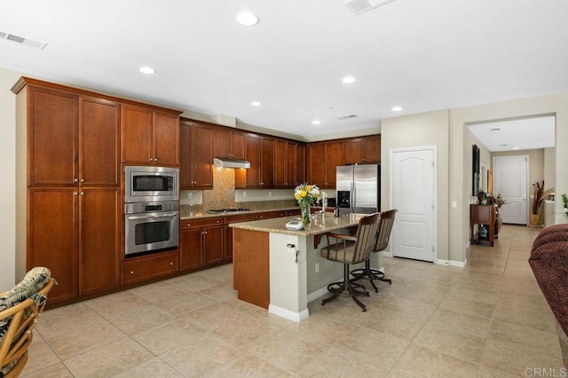 kitchen featuring visible vents, a kitchen bar, under cabinet range hood, backsplash, and stainless steel appliances