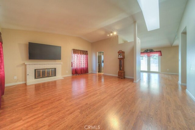 24731 Huntley Dr, Moreno Valley, CA 92557 - unfurnished living room featuring vaulted ceiling with skylight, baseboards, a brick fireplace, and light wood-style flooring