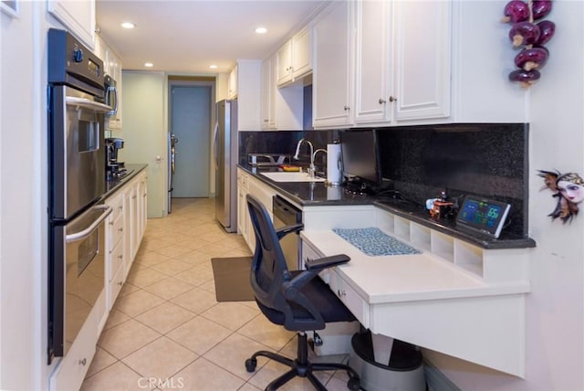 kitchen with decorative backsplash, a sink, light tile patterned floors, stainless steel appliances, and white cabinetry