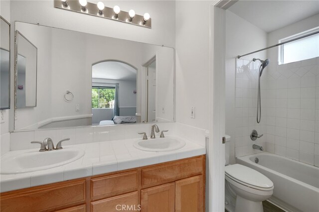 ensuite bathroom with double vanity, toilet, bathing tub / shower combination, and a sink