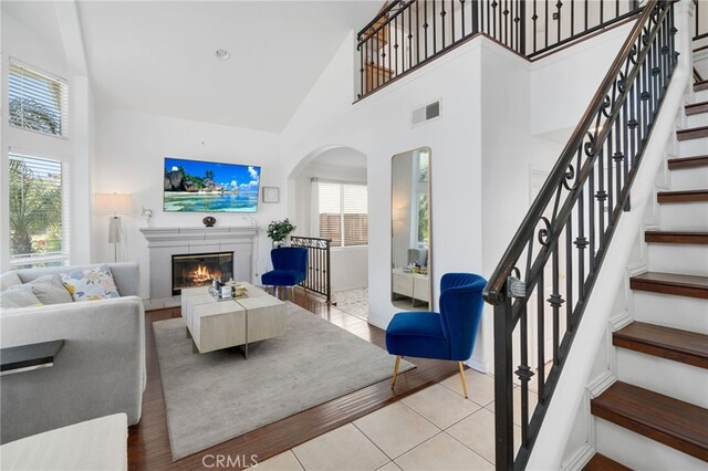 living area featuring visible vents, arched walkways, a glass covered fireplace, and high vaulted ceiling
