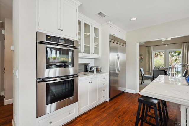 kitchen with visible vents, baseboards, glass insert cabinets, stainless steel appliances, and dark wood-type flooring