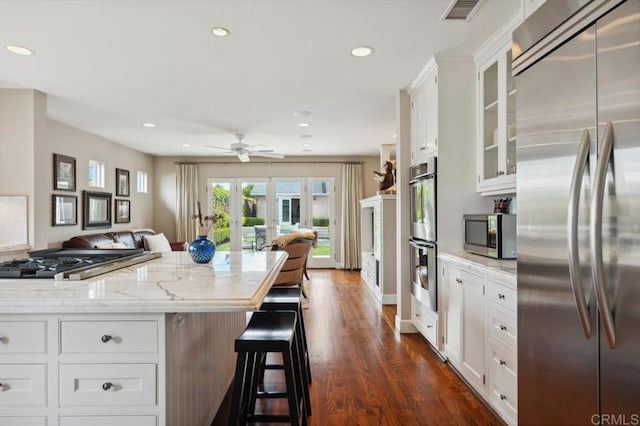kitchen featuring a breakfast bar area, stainless steel appliances, recessed lighting, visible vents, and glass insert cabinets