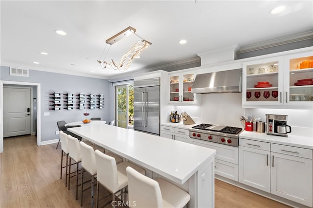 207 Via Galicia, San Clemente, CA 92672 - kitchen with wall chimney range hood, stainless steel appliances, ornamental molding, a breakfast bar, and light countertops