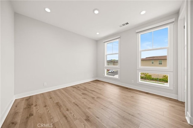 empty room with baseboards, visible vents, and light wood finished floors