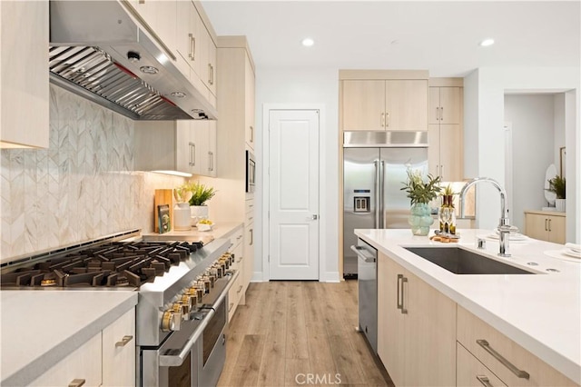 kitchen with a sink, light wood-style floors, built in appliances, light countertops, and under cabinet range hood