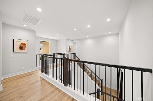 corridor featuring visible vents, wood finished floors, baseboards, recessed lighting, and an upstairs landing