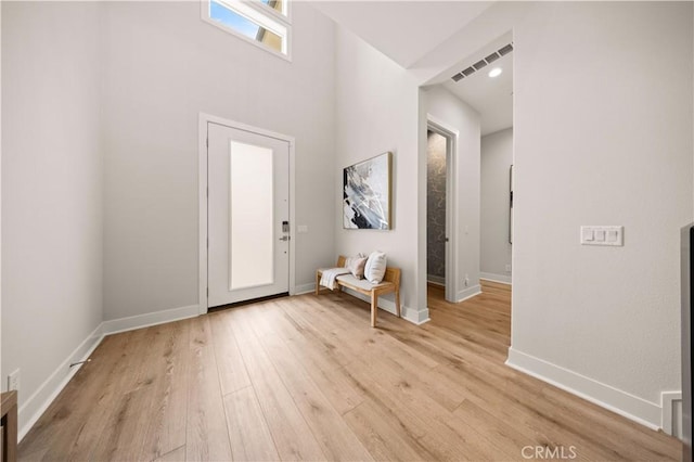 entrance foyer with a towering ceiling, baseboards, visible vents, and light wood-style floors