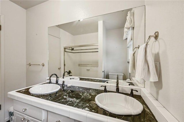 bathroom featuring double vanity, toilet, a shower stall, and a sink