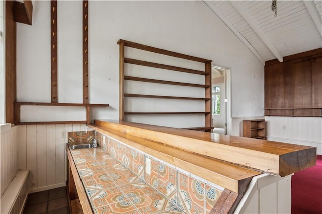 bar featuring lofted ceiling with beams, bar, a sink, a wainscoted wall, and dark tile patterned flooring
