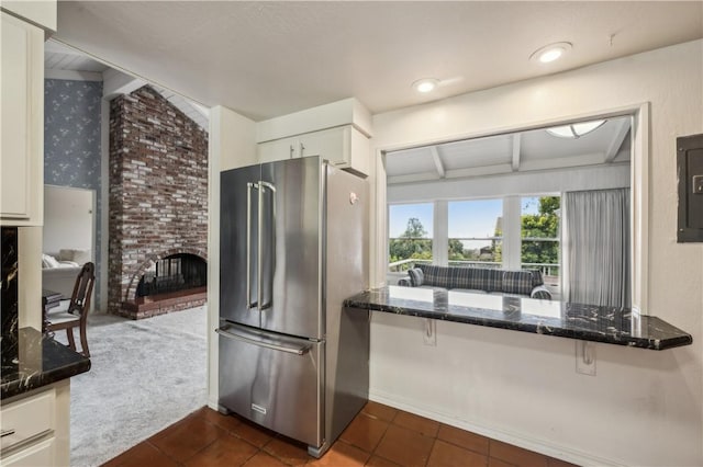 kitchen with high end fridge, a brick fireplace, dark stone counters, white cabinetry, and dark tile patterned flooring