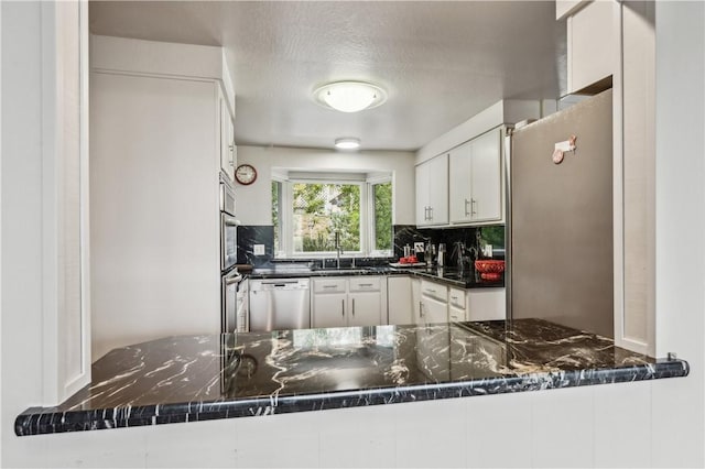 kitchen with white cabinets, appliances with stainless steel finishes, a sink, dark stone countertops, and backsplash