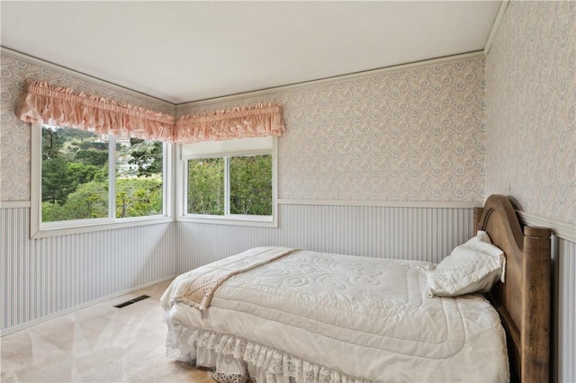 carpeted bedroom featuring wallpapered walls, visible vents, and a wainscoted wall