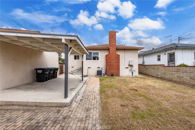back of house featuring a yard, fence, a chimney, and stucco siding