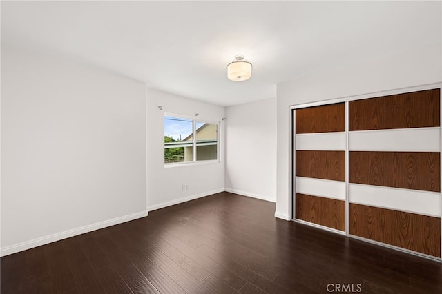 unfurnished bedroom featuring baseboards, wood finished floors, and a closet