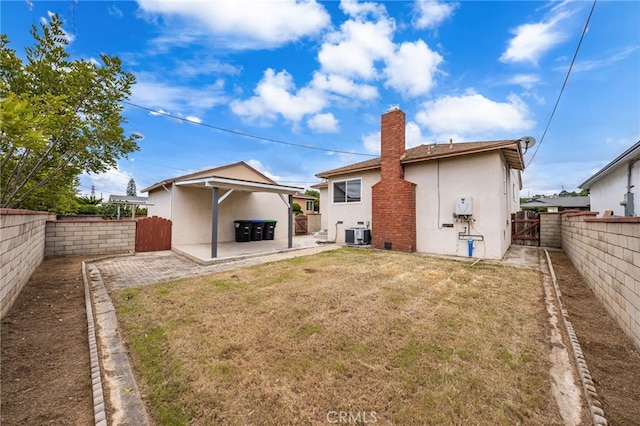 rear view of property with a fenced backyard, stucco siding, a gate, central AC unit, and a lawn