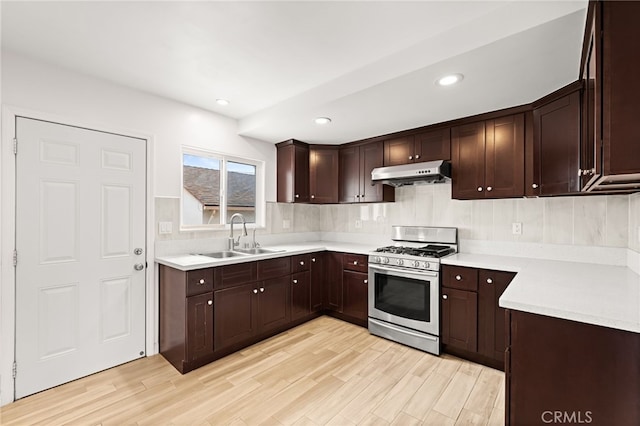 kitchen featuring dark brown cabinetry, a sink, stainless steel gas stove, light countertops, and under cabinet range hood