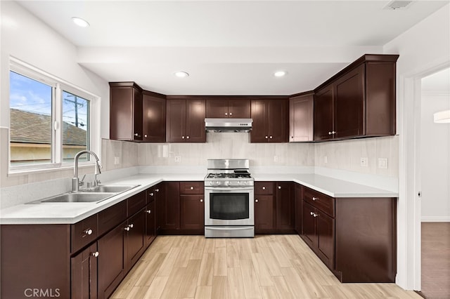 kitchen featuring a sink, light countertops, stainless steel gas range oven, and under cabinet range hood