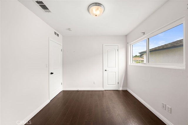 spare room featuring baseboards, dark wood-style floors, and visible vents