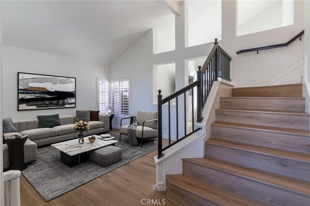 living area with high vaulted ceiling, wood finished floors, and stairway