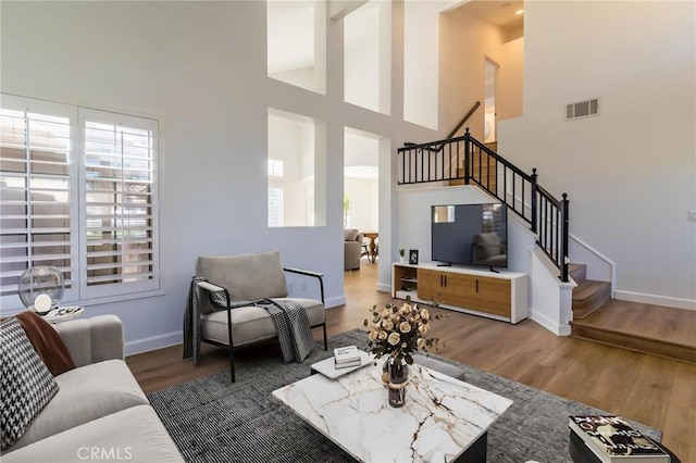 living area featuring a high ceiling, stairs, baseboards, wood finished floors, and visible vents