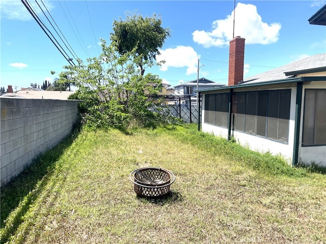 view of yard featuring a fenced backyard, a sunroom, and an outdoor fire pit