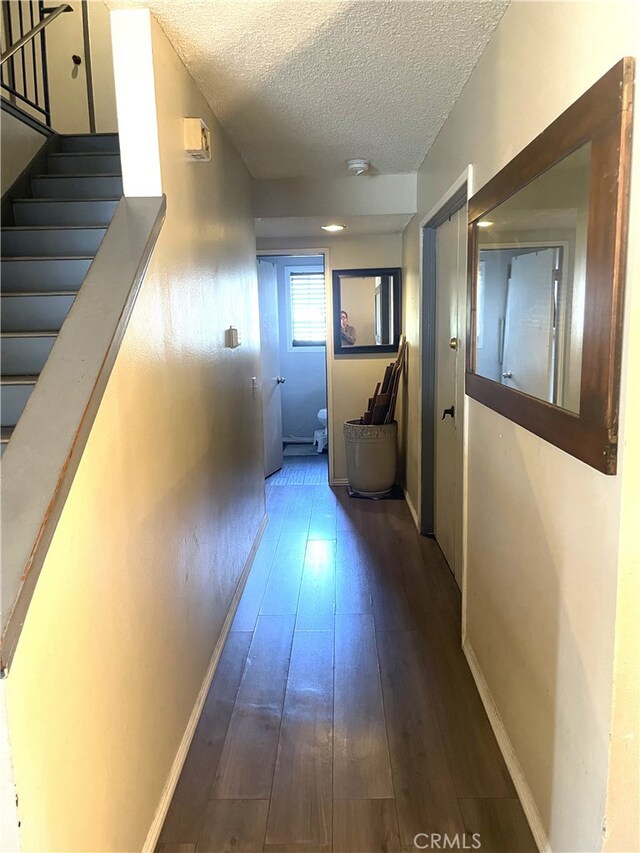 corridor featuring wood-type flooring, a textured ceiling, baseboards, and stairway