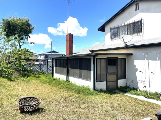 rear view of house with a chimney, a lawn, a sunroom, fence, and stucco siding