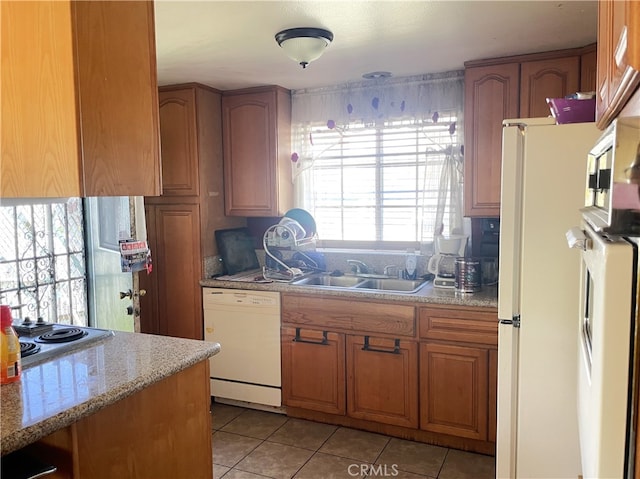 kitchen featuring light tile patterned flooring, light stone counters, a sink, white appliances, and brown cabinetry