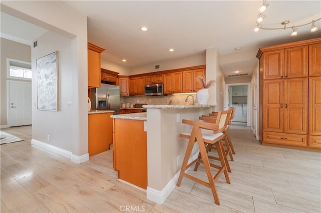 56 Egret Ln, Aliso Viejo, CA 92656 - kitchen with appliances with stainless steel finishes, independent washer and dryer, brown cabinetry, a peninsula, and light stone countertops