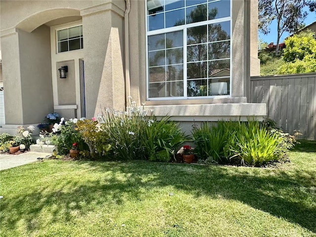 view of exterior entry featuring a lawn, fence, and stucco siding