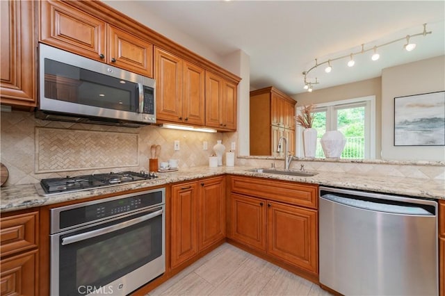 kitchen featuring a sink, appliances with stainless steel finishes, brown cabinetry, and light stone countertops