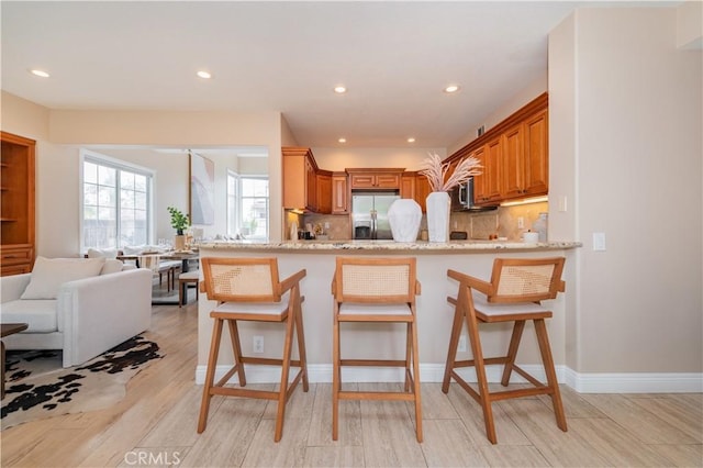 56 Egret Ln, Aliso Viejo, CA 92656 - kitchen with stainless steel appliances, brown cabinetry, a peninsula, tasteful backsplash, and light wood-style flooring