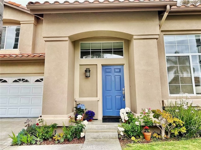 view of exterior entry with stucco siding, an attached garage, and a tiled roof