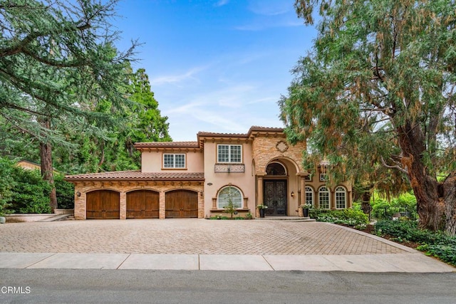 mediterranean / spanish-style house with a tiled roof, decorative driveway, stone siding, and stucco siding