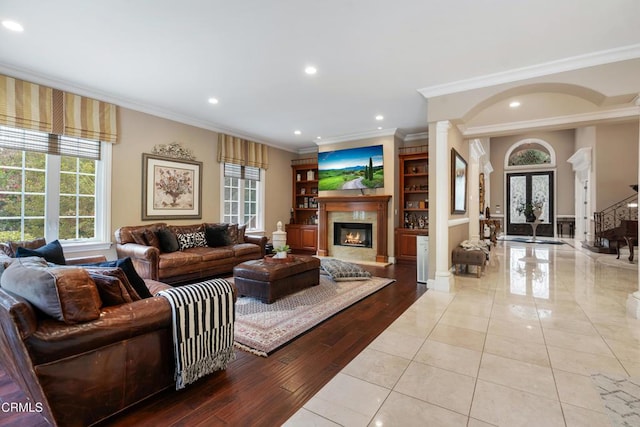 tiled living room with crown molding, a healthy amount of sunlight, ornate columns, and a premium fireplace