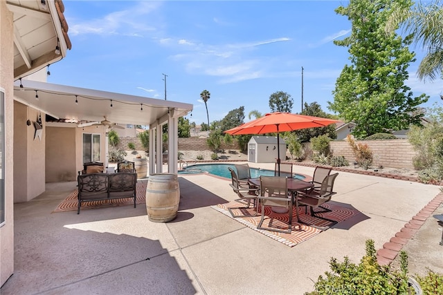 view of pool featuring a patio, outdoor dining area, a fenced backyard, a storage shed, and an outbuilding