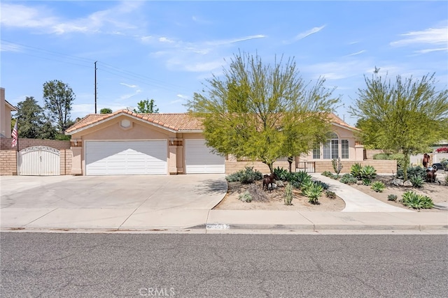 view of front of house featuring a garage, stucco siding, a gate, a tiled roof, and concrete driveway