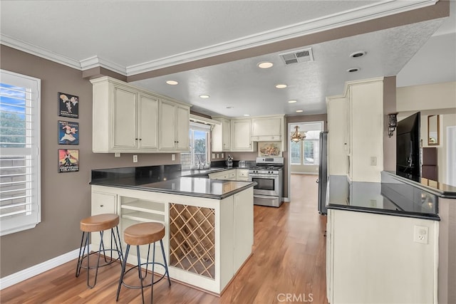 kitchen featuring visible vents, dark countertops, a peninsula, light wood-style floors, and stainless steel appliances