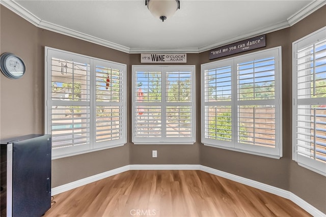 unfurnished dining area with baseboards, ornamental molding, and wood finished floors