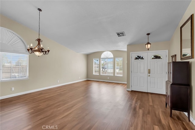 entrance foyer with a notable chandelier, vaulted ceiling, wood finished floors, and visible vents