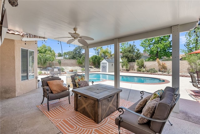 view of pool featuring ceiling fan, a storage shed, a patio area, a fenced backyard, and an outdoor fire pit