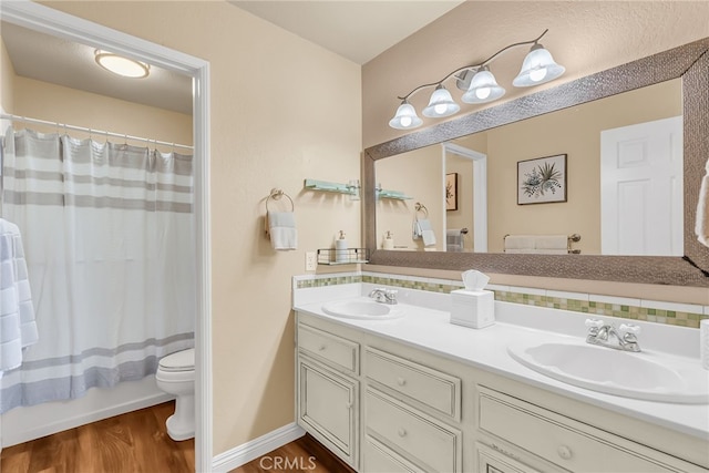 bathroom featuring double vanity, a sink, wood finished floors, and toilet