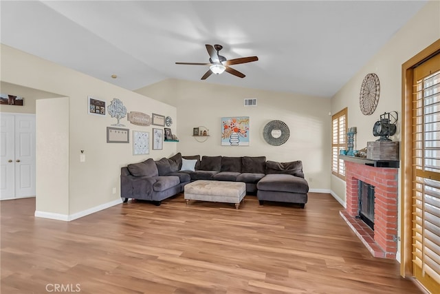 living area with ceiling fan, a fireplace, lofted ceiling, light wood-type flooring, and visible vents