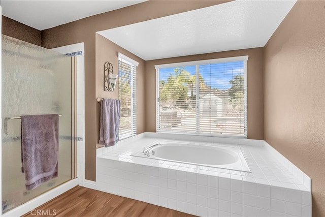 bathroom featuring a garden tub, a textured wall, a stall shower, and wood finished floors