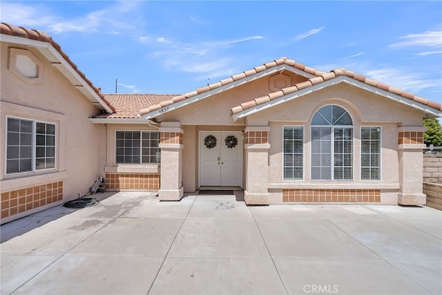 entrance to property featuring a tiled roof, a patio area, and stucco siding