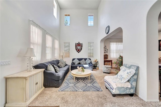 carpeted living room with arched walkways and a towering ceiling