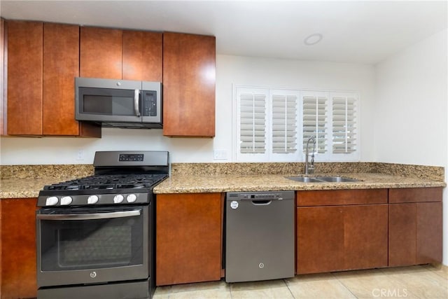 kitchen featuring stainless steel appliances, a sink, brown cabinetry, and light stone counters