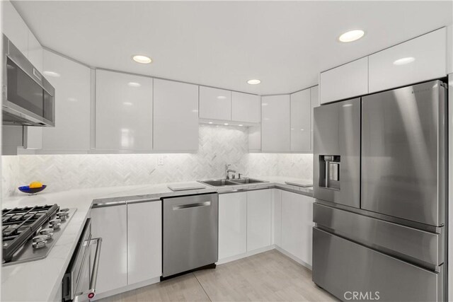 kitchen featuring white cabinets, appliances with stainless steel finishes, a sink, light countertops, and modern cabinets