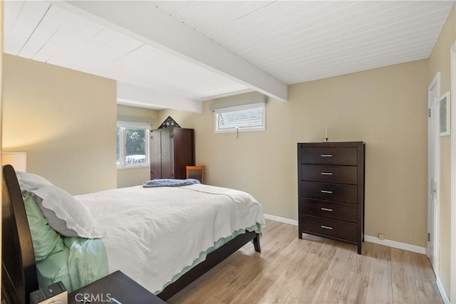 bedroom with beamed ceiling, baseboards, multiple windows, and light wood-type flooring